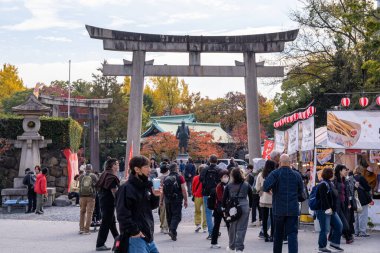 Günbatımında Japonya 'da bir sonbahar festivali sırasında, Osaka, Japonya - 24 Kasım 2025' te gıda tezgahları ve renkli dekorasyonlarla kalabalık bir tapınak girişinde toplandı.
