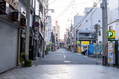 23 Kasım 2025 Osaka Japonya: Sabahın erken saatlerinde boş dükkanları ve park etmiş arabaları olan bir şehirde sakin bir cadde