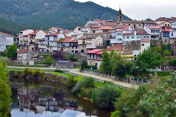Nehir ve yürüyüş yolu olan kırsal bir dağ köyünde kilise ve evler. Bazı evler nehre yansıyor.