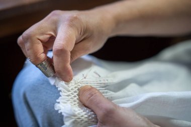 Eller, iğne, iplik ve yüksük kullanarak beyaz kumaşa dikiş atıyor.