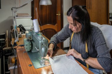 Mekanik dikiş makinesinde dikiş dikmeye odaklanan bir kadın, mezurayla çalışıyor.