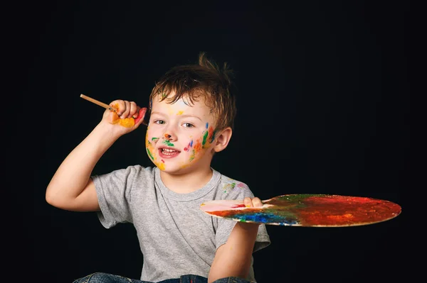Мальчик с раскрашенными в яркие цвета руками, с палитрой в руке — стоковое фото