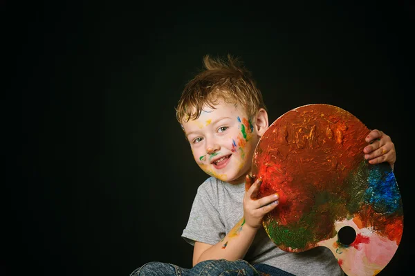 Мальчик с раскрашенными в яркие цвета руками, с палитрой в руке — стоковое фото