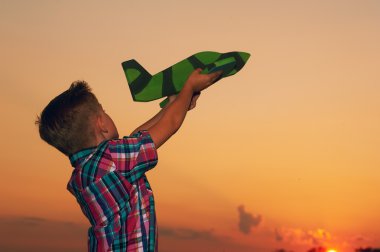 Gün batımı arka plan üzerinde oyuncak uçak ile oynayan mutlu çocuk