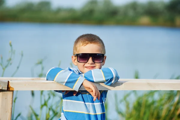 Mooie jongen poseren zittend op een houten brug. Gekleed in een nautisch thema . — Stockfoto