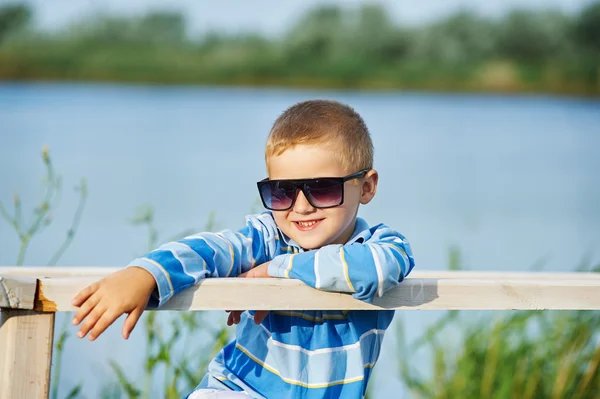 Mooie jongen poseren zittend op een houten brug. Gekleed in een nautisch thema . — Stockfoto