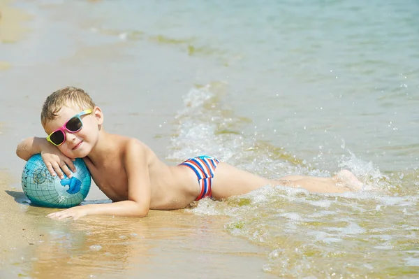 Niño en la playa con la pelota que representa el mundo — Foto de Stock