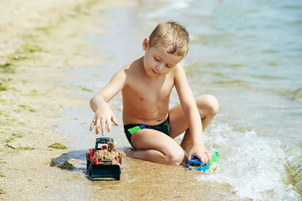 Un niño juega con coche de juguete en la playa —  Fotos de Stock