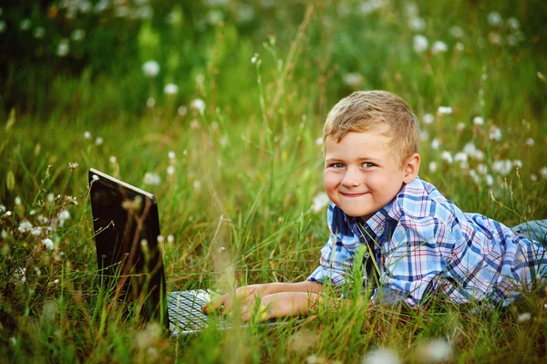 Junge auf Feld mit Löwenzahn mit Laptop — Stockfoto