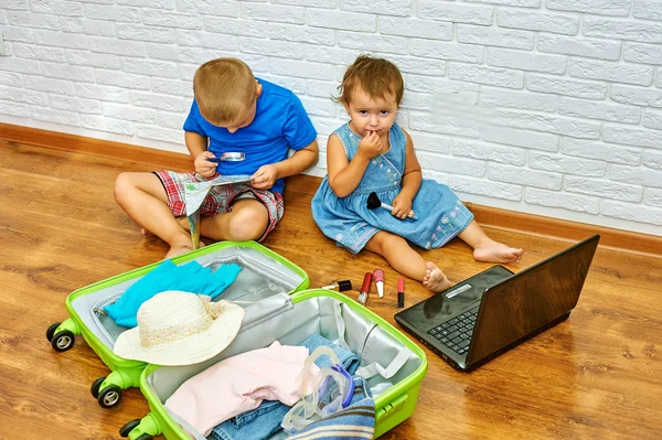 Брат і сестра сидять на підлозі біля валізи, вивчаючи карту і дивлячись на ноутбук — стокове фото