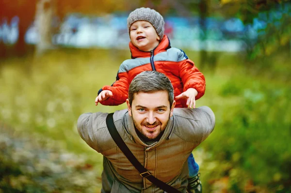 Счастливый молодой отец играет с сыном в осеннем парке — стоковое фото