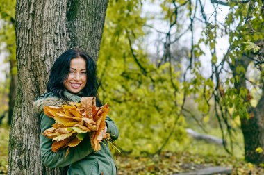 Sonbaharda akçaağaç gülümseyen genç çekici kadın parkta düşüş açık havada kalıyor.