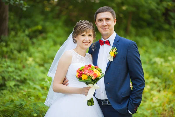 Happy bride, groom standing in green park, kissing, smiling, laughing — Stock Photo, Image