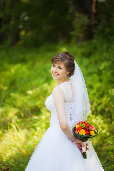 Schöne Braut am Hochzeitstag mit einem Strauß im Park — Stockfoto