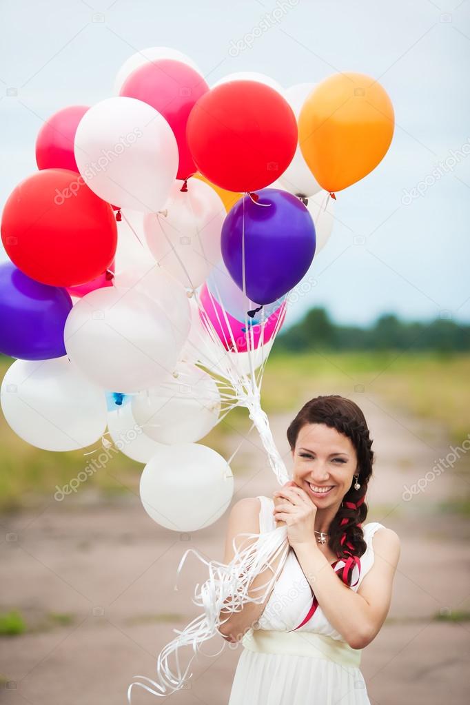 Happy young woman holding in hands colorful latex balloons outdo