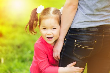 Little girl cheerfully hugging leg of mother
