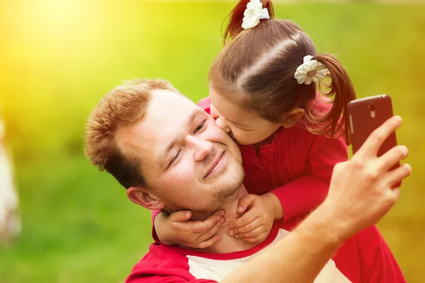 Little girl kissing her father on cheek while taking selfie — ストック写真