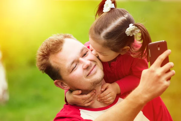 Little girl kissing her father on cheek while taking selfie — 图库照片