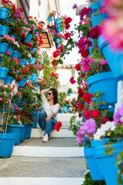 Endülüs verandasında saksı ve çiçeklerle dolu bir merdivende oturan güzel bir kadın.