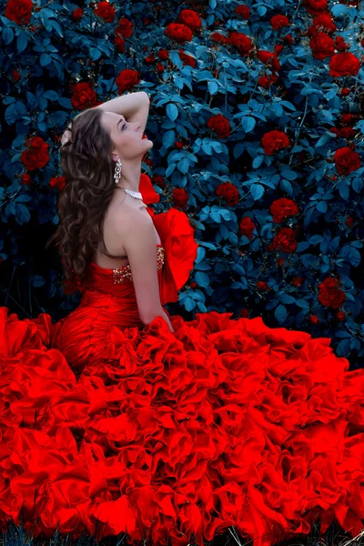Schöne junge Dame im roten Kleid steht auf Blume Rose — Stockfoto