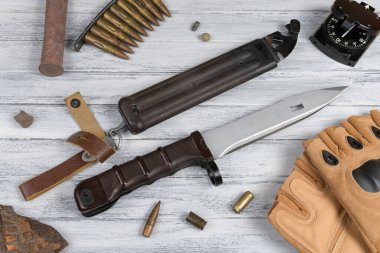 Süngü, taktik eldiven, pusula, fişekli şarjör, fişek kovanı ve tahta arka planda bir topçu mermisinden kıymık.