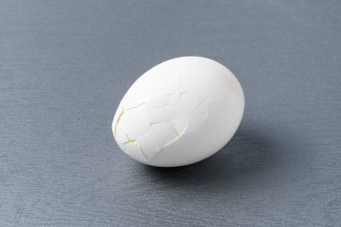 Kırık haşlanmış yumurta, kabuğunda çatlaklar olan gri bir kesme tahtası.