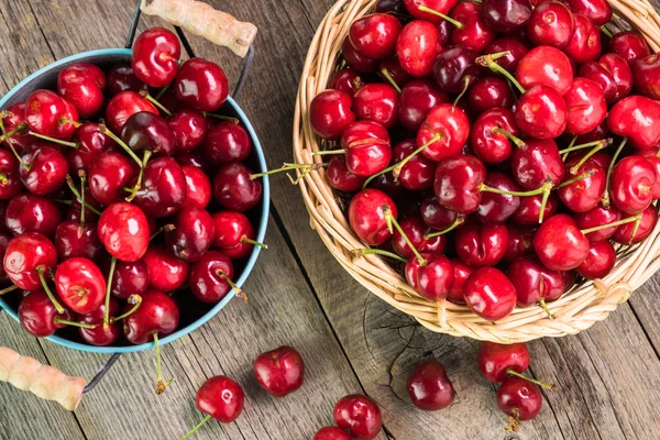 Rote Kirschen in Metalleimer und Korb auf Holzgrund. — Stockfoto