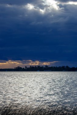 Gölün üzerinde kara bulutlarla gün batımının dramatik görüntüsü