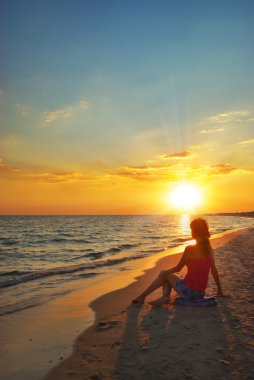 Kız sahilde oturuyor.