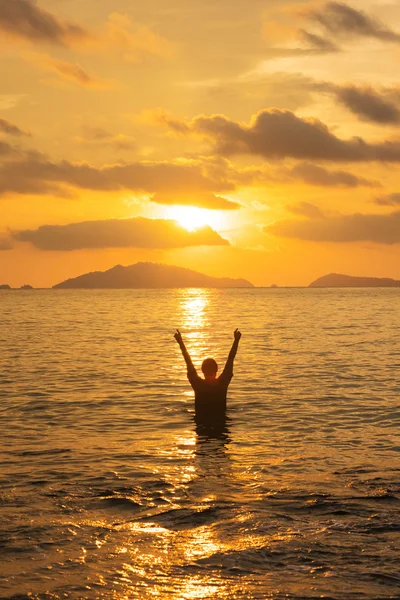 Femme debout sur la mer au coucher du soleil avec la main levée — Photo