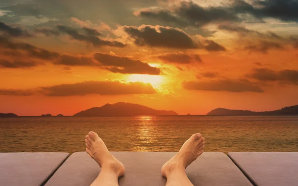 Férfi láb pihentető, napozó ágy, naplemente a strandon — Stock Fotó