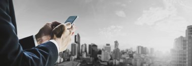 Güneş doğarken iş bölgesinde şehrin panoramik cityscape cep telefonu kullanarak iş adamı