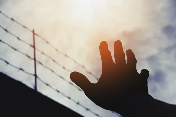 Mano de silueta extendiéndose al cielo con desenfoque barbwire, en el sombrío cielo nublado —  Fotos de Stock