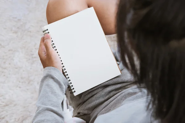 Asiático cara segurando notebook em branco com lápis na sala de estar — Fotografia de Stock