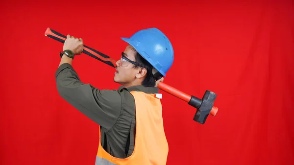 asian construction worker man wearing uniform, helmet, with hammer isolated red backgroubd