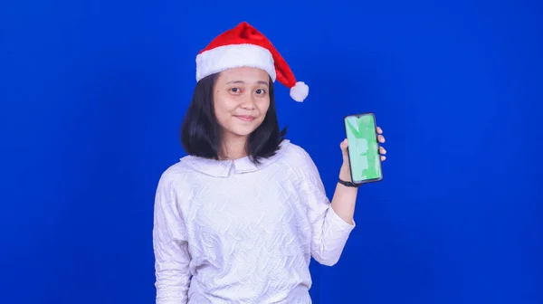 緑の画面の携帯電話を保持クリスマスの帽子を身に着けているアジアの女性は青の背景 — ストック写真
