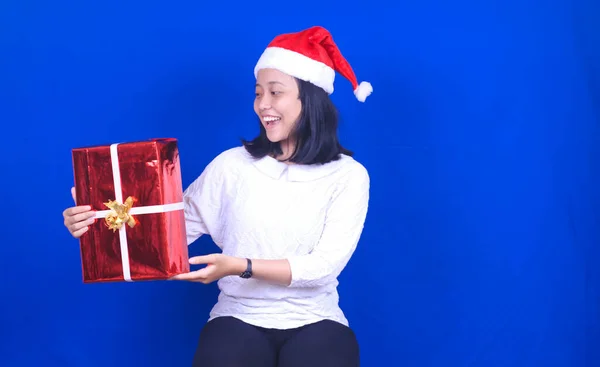 クリスマスの帽子をかぶっているアジアの女性は贈り物をもたらす隔離された青の背景 — ストック写真
