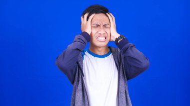 Baş ağrısı ceketi giyen Asyalı adam mavi arka planda.