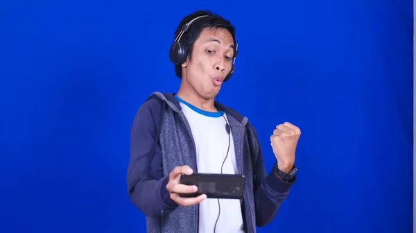 Azjatycki Człowiek Gra Mobilna Gra Szczęśliwy Wyrażenie Odizolowane Niebieskie Tło — Zdjęcie stockowe