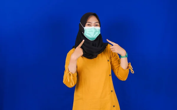 Asian hijab woman pointing mask isolated blue background