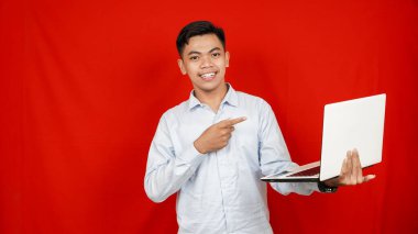 Asyalı iş adamı, kırmızı arka planda dizüstü bilgisayarı işaret ediyor