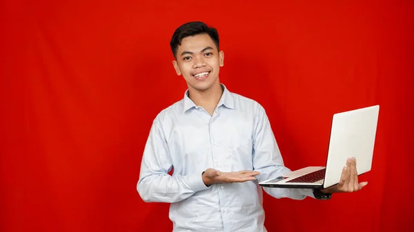 亚洲商人指着桌子上的笔记本电脑 孤立的红色背景 — 图库照片