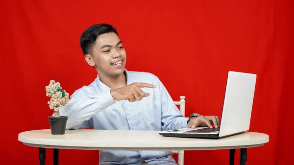 Asyalı Adamı Kırmızı Arka Planda Dizüstü Bilgisayarı Işaret Ediyor — Stok fotoğraf