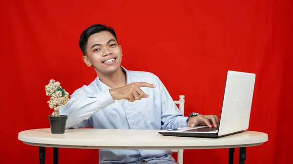 Asian business man pointing laptop on table isolated red background