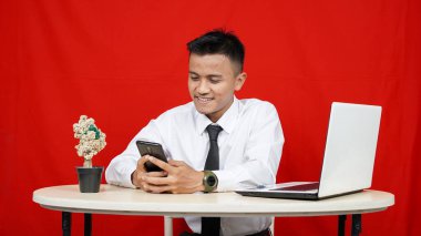 Genç Asyalı iş adamı gülümsüyor. Bilgisayarlı cep telefonu kırmızı arka planda.