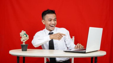 Asyalı iş adamı, kırmızı arka planda dizüstü bilgisayarı işaret ediyor