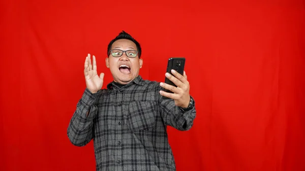 Wow face of Asian man shocked what he see in the smartphone isolated red background