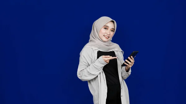 Ásia Hijab Mulher Apontando Handphone Sorriso Expressão Isolado Azul Fundo — Fotografia de Stock