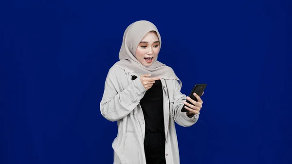 Asiática Hijab Mujer Señalando Teléfono Móvil Sonrisa Expresión Aislado Azul —  Fotos de Stock