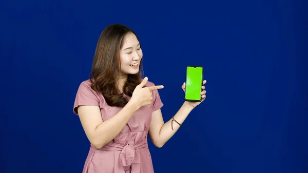 Beautiful Asian Woman Pointing Green Screen Handphone Isolated Blue Background — Stock Photo, Image